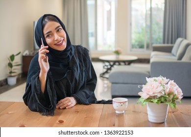 Smiling young muslim woman talking on mobile phone while enjoying morning coffee at home - Powered by Shutterstock
