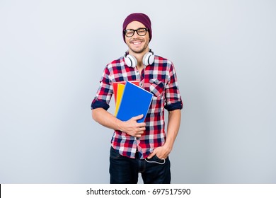 Smiling young nerdy stylish student hipster is standing with books on pure background in black trendy glasses and hat, casual bright checkered outfit