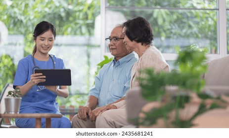 A smiling young nurse assists an elderly couple with technology, showing them information on a tablet in a bright, plant-filled room. - Powered by Shutterstock