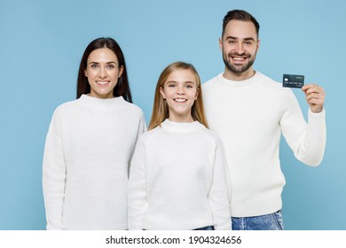 Smiling Young Parents Mom Dad With Child Kid Daughter Teen Girl In Casual White Sweaters Hold Credit Bank Card Isolated On Blue Background Studio Portrait. Family Day Parenthood Childhood Concept