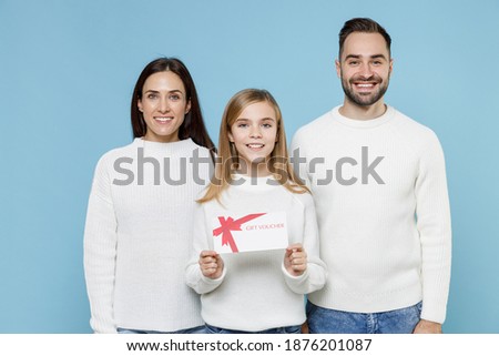 Smiling young parents mom dad with child kid daughter teen girl in casual white sweaters hold gift certificate isolated on blue background studio portrait. Family day parenthood childhood concept