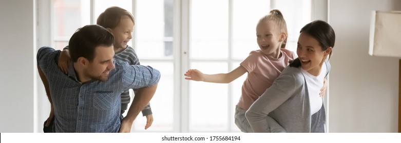 Smiling Young Parents Piggy Backing Laughing Adorable Little Son And Daughter Wide Horizontal Banner, Happy Family Having Fun, Running, Dancing In Living Room, Enjoying Leisure Time Together