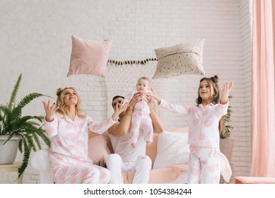 Smiling Young Parents, Their Two Daughters Have Fun At Home And Throw Pillows In A Bright Interior