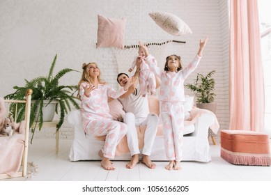 Smiling Young Parents, Their Two Daughters Have Fun At Home And Throw Pillows In A Bright Interior