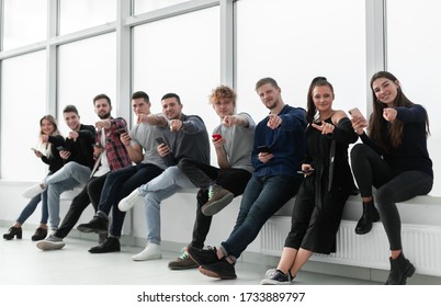 smiling young people with smartphones sitting near an office window.