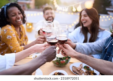 Smiling young people toasting red wine at rooftop barbecue. Gathered colleagues drinking and eating outdoors. Group of diverse friends enjoying free time on vacation. Relationships and celebrations. - Powered by Shutterstock