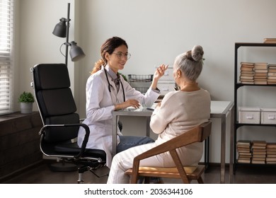 Smiling young physician giving advice, talking to senior woman at appointment in office. Old patient visiting doctor, consulting practitioner about treatment, complaining of geriatric health problem - Powered by Shutterstock