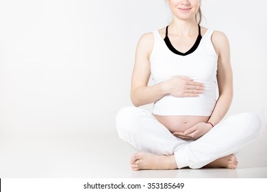 Smiling Young Pregnant Fitness Model In Sportswear Doing Yoga Or Pilates Training, Sitting In Easy Pose, Sukhasana, Touching Her Belly, Breathing, Gray Background, Studio Shot, Close-up, Copy Space