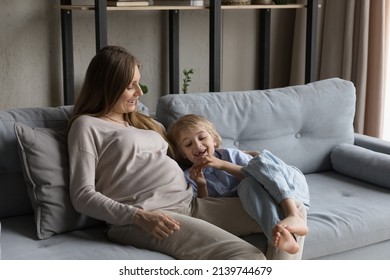 Smiling young pregnant mother with big belly playing with cute small kid son, talking resting on comfortable couch at home, enjoying carefree weekend pastime, family communication, childcare concept.