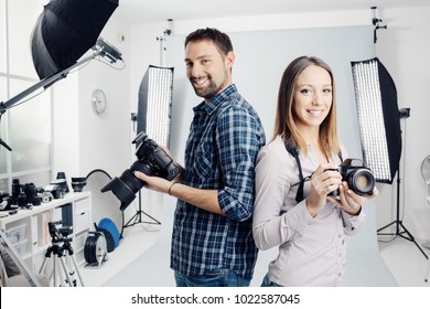 Smiling young professional photographers posing in the studio, they are holding digital cameras - Powered by Shutterstock