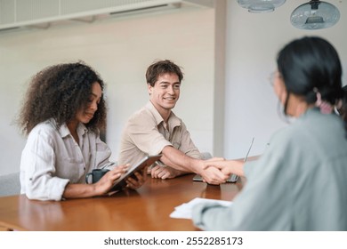 Smiling young professionals of diverse backgrounds engage in a handshake, signaling the start of a business meeting in a contemporary office setting, while dressed in smart casual attire. - Powered by Shutterstock