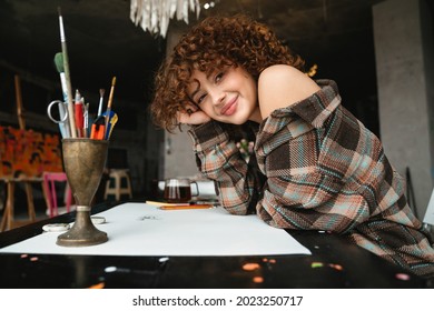 Smiling Young Redhead Woman Artist Drawing With Pencil Sitting At The Desk With Cup Of Tea In The Studio Workshop