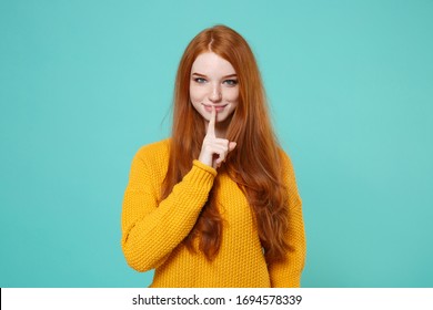 Smiling young redhead woman girl in yellow sweater isolated on blue turquoise background in studio. People lifestyle concept. Mock up copy space. Saying hush be quiet with finger on lips shhh gesture