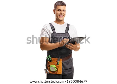 Smiling young repairman with a tool belt writing on a clipboard isolated on white background