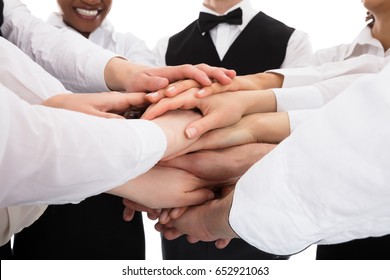 Smiling Young Restaurant Staff Stacking Hands Over White Background