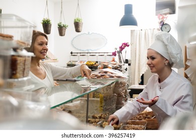 Smiling Young Shop Woman Offering Senior Client Nuts And Smiling 