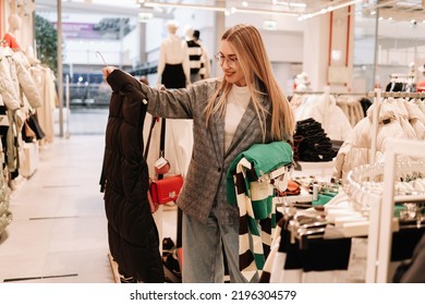 A smiling young shopaholic woman tries on clothes in a shopping mall store, walks through boutiques. Consumerism is a modern problem of society. Selective focus