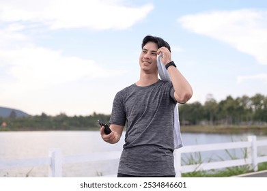 Smiling young sport man wiping sweat with towel while resting after a running by the lake - Powered by Shutterstock