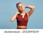 Smiling young sporty woman closing eyes wearing sportwear posing in studio, isolated on blue. Sport, health care, wellness concept