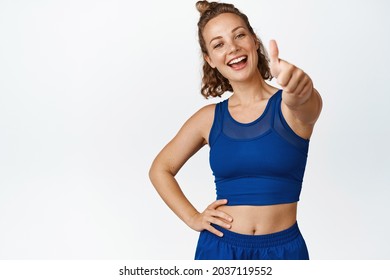 Smiling young spportswoman shows thumbs up. Motivated fitness woman like something, giving compliment, recommending sport gym, white background. - Powered by Shutterstock