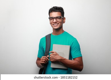 Smiling young student of Indian origin carrying shoulder bag and a book
