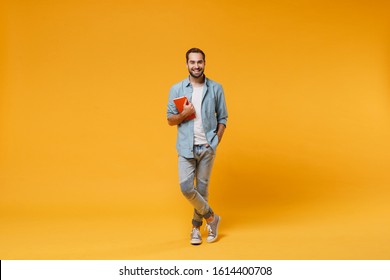Smiling young student man in casual blue shirt posing isolated on yellow orange wall background studio portrait. People sincere emotions lifestyle concept. Mock up copy space. Holding red notebook