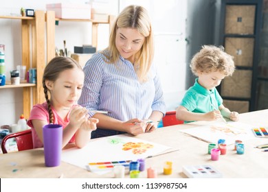 Smiling young teacher drawing with paints and teaching her pupils to paint - Shutterstock ID 1139987504
