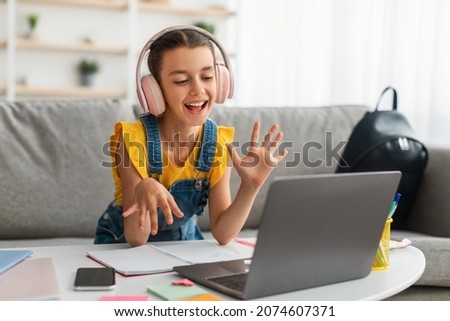 Smiling young teen girl wearing wireless headphones video calling on pc laptop. Happy female student looking at computer screen watching webinar or doing video chat by webcam with friends or teacher