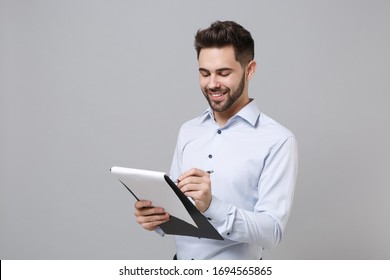 Smiling Young Unshaven Business Man In Light Shirt Posing Isolated On Grey Background. Achievement Career Wealth Business Concept. Mock Up Copy Space. Hold Clipboard With Papers Document Write Notes