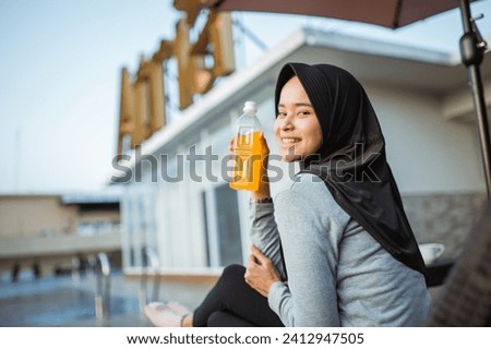 smiling young veiled woman in sportswear holding a drink bottle by the pool