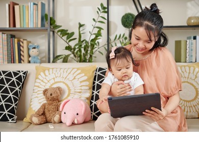 Smiling Young Vietnamese Woman Staying Home With Baby Girl And Showing Her Educational Video On Tablet Computer