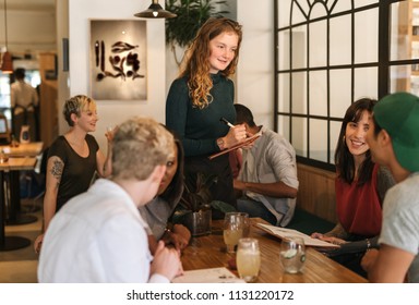 Smiling young waitress taking orders from a diverse group of customers sitting at a table in a bistro - Powered by Shutterstock