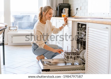 Smiling young white woman putting dishes in the dishwasher at home