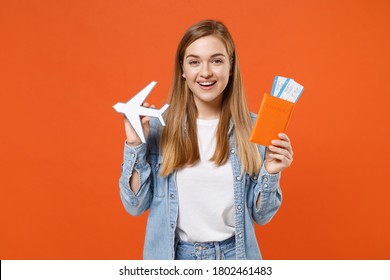 Smiling Young Woman 20s In Casual Denim Clothes Posing Isolated On Orange Background Studio Portrait. People Lifestyle Concept. Mock Up Copy Space. Hold Passport Ticket Boarding Pass Paper Airplane