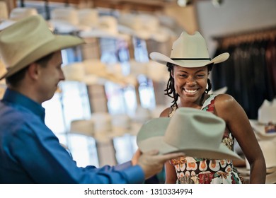 Smiling Young Woman Admires The Hat Shown To Her By The Owner Of The Cowboy Hat Shop.