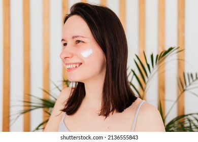 Smiling Young Woman Applying Cream On Face At Home. Morning Beauty Routine. Skincare Concept