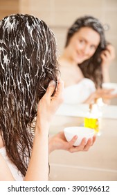 Smiling Young Woman Applying Hair Mask In Front Of A Mirror; Haircare Concept