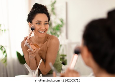 Smiling Young Woman Applying Makeup In Front Of Mirror, Putting On Face Powder, Blusher Or Bronzer At Home, Copy Space. Decorative Cosmetics, Beauty And Skin Care Concept