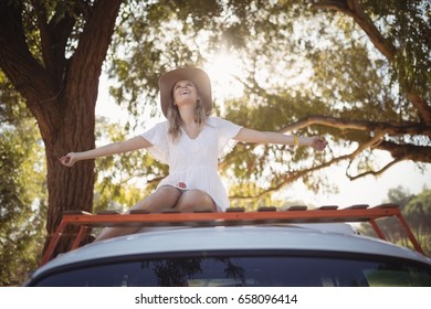 Smiling young woman with arms outstretched sitting on van - Powered by Shutterstock