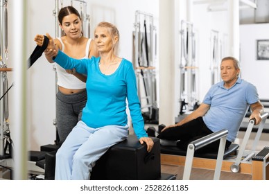 Smiling young woman assisting senior woman training on Pilates bed machine in rehabilitation center - Powered by Shutterstock