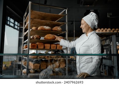 Smiling young woman baker in uniform taking bread from rack - Powered by Shutterstock