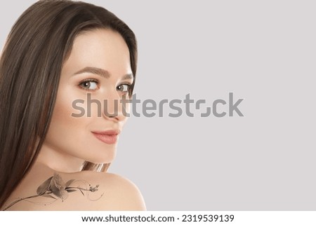 Smiling young woman with beautiful flower tattoo on light background, space for text