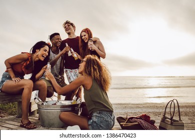 Smiling young woman with beer bottle and friends standing by on the beach. Friends group having a party on the beach in evening - Powered by Shutterstock