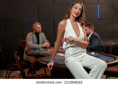 Smiling Young Woman With Betting Chips Sitting On Edge Of Poker Table