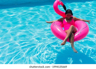 Smiling young woman in bikini relaxes on inflatable pink flamingo in swimming pool. Attractive woman in swimsuit lies in the sun on tropical vacation. Woman sunbathing at the resort.