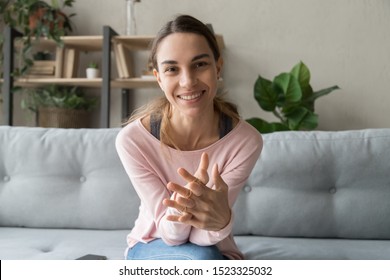 Smiling young woman blogger influencer sit on sofa looking at camera make video conference call recording vlog at home, happy girl vlogger do online chat shooting blog at home, portrait, webcam view