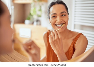 Smiling young woman brushing teeth in bathroom. Girl looking in mirror while using ecological toothbrush with whitening toothpaste to clean her teeth. Multiethnic girl cleaning teeth in the morning. - Powered by Shutterstock