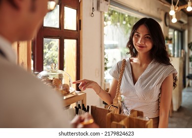 Smiling Young Woman Buying Fresh Croissants In Coffeeshop For Breakfast