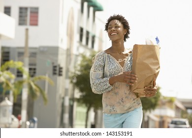 Smiling young woman carrying grocery bag while walking on street