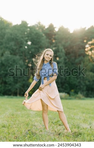 Smiling young woman in casual clothes strolls through the park. She is holding shoes in her hands. She is free and happy. The concept of freedom and youth